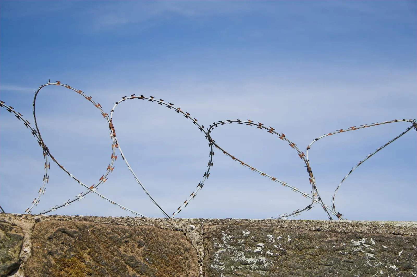 Coils of razor wire on top of a stone wall against a blue sky