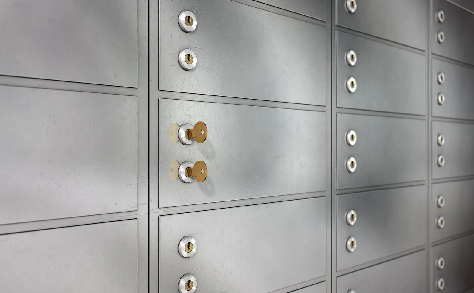 Wall of metal safe deposit boxes, two with a golden key inserted in the lock